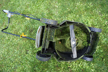 The electric lawn mower lies on the grass upside down with wheels.の写真素材