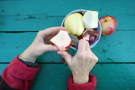 The elderly gardener  woman cleans the skins from  apples to eat fruitsの写真素材