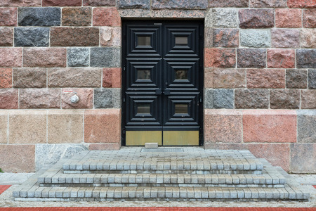A closed wooden aged blue oak door of a red granite stone wall in public building.の写真素材