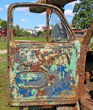 The open door of an old rusty agricultural farm truck that was thrown near the village background. Sunny summer dayの写真素材