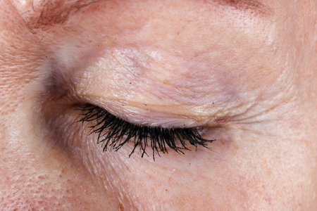 Closed eye and eyelashes with lumps of black ink mascara from an old seniior elderly  woman.  Macro concept shotの写真素材