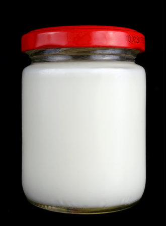 Small one hundred gram glass jar with white milk and a red lid. Isolated on black studio macroの写真素材