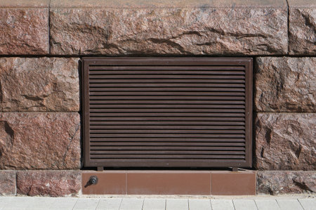 Metal grille of a ventilation shaft in a wall made of  granite stonesの写真素材