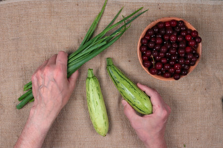 An elderly country man thinks about what to cook with green onions, zucchini   and frozen cherriesの写真素材