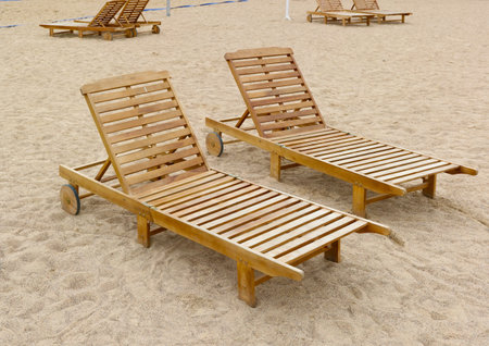 Empty wooden beach sun lounges on a sandy lake  bank.