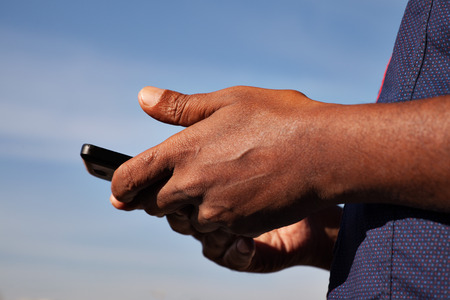 black men's hands holding phone blue sky behindの写真素材