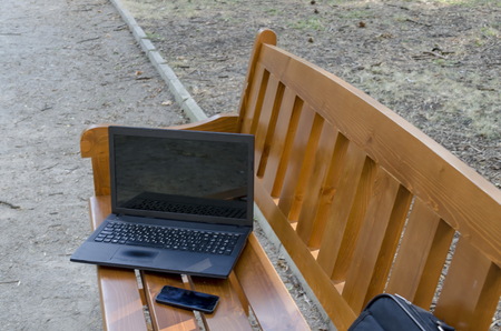 Open laptop computer, bag and phone  on  wooden bench in the park, Sofia, Bulgariaの写真素材