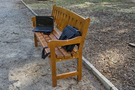 Open laptop computer, bag and phone  on  wooden bench in the park, Sofia, Bulgariaの写真素材