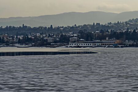 Winter scene with frozen lake, snowy mountain, glade, forest and residential district of bulgarian village Pancharevo, Sofia, Bulgariaの写真素材