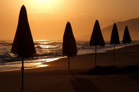 Folded sunshades early in the morning on the beach in sunshine, island of Crete, Greeceの写真素材