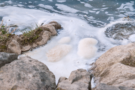 Polluted river, foam in a water near shore.