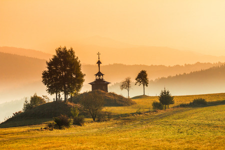 Wooden chapel in an autumn landscape, sunrise in a foggy morning, Slovakia, Europe.の写真素材
