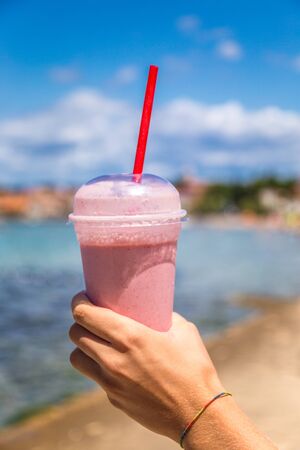 Milkshake held in hand on blurred background of sea resort in sunny day.の写真素材
