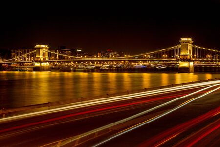 The famous SzÃ©chenyi Chain Bridge in Budapest, Hungary, illuminated above the Danube river. Long exposure with light trails of cars at a night.の写真素材