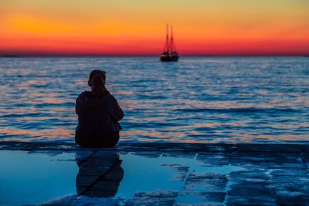 Silhouette of a young woman looking out to sea at sunset. Adriatic Sea at Zadar town, Croatia,...