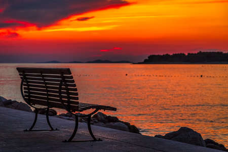 Sea landscape at sunset with bench in Primosten town, a popular tourist destination on the Dalmatian coast of Adriatic sea in Croatia, Europe.の写真素材