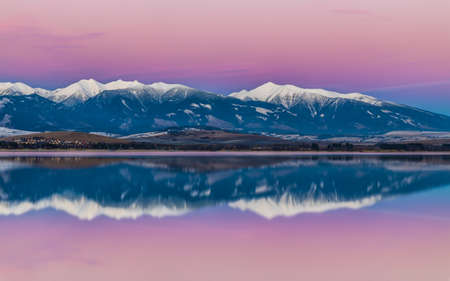 Winter landscape at sunset. Snow-capped mountains reflected in the lake. Liptovska Mara dam with the Western Tatras mountain in the background, Slovakia, Europe.の写真素材