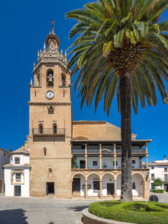 Ronda town in Spain. Historic church tower and plaza with palm tree under a bright blue sky.の写真素材