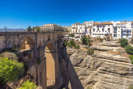 The Puente Nuevo bridge in El Tajo gorge in Ronda town in Spain. Ancient stone bridge spanning a deep gorge, overlooking a picturesque town nestled on a cliffside. Sunny day.の写真素材