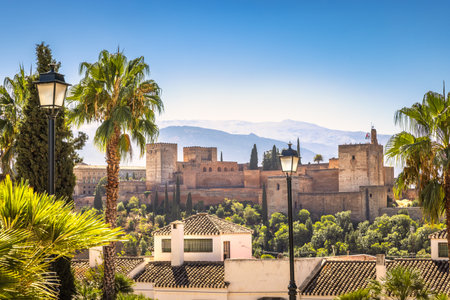 The Alhambra palace from viewpoint in Granada town in Spain. Historic castle nestled in a sunny, palm-tree filled landscape, mountains in the background.の写真素材