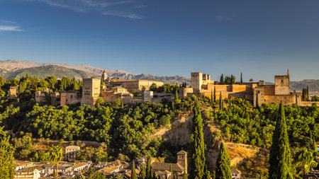 Panorama of Alhambra from the Mirador de San Nicolas viewpoint in Granada town in Spain at sunset. Ancient fortress and palace nestled on a hilltop, overlooking a town and mountains under a clear sky.の写真素材
