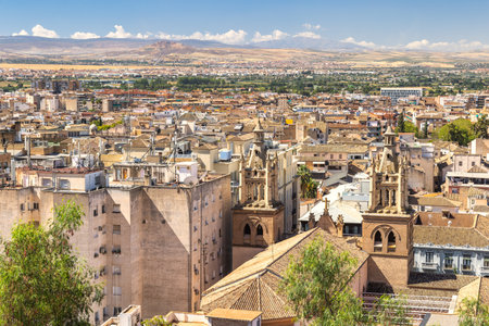 Granada town in Spain. Panoramic view of a city nestled in a valley, with mountains in the background. Buildings are primarily tan and low-rise, with some taller structures.の写真素材