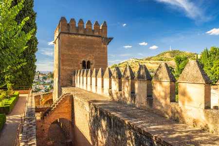 Alhambra complex in Granada town, Andalusia, Spain. Ancient fortress walls and tower overlooking a cityscape under a vibrant blue sky.の写真素材