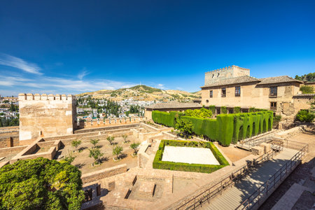 The Mexuar, part of the Alhambra complex, Granada, Andalusia, Spain. Ancient palace gardens with manicured hedges and a stone tower under a clear blue sky.の写真素材