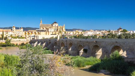 Roman bridge in Cordoba town in Spain. Ancient stone bridge spanning a river, with a historic city and grand architecture in the background under a clear blue sky.の写真素材
