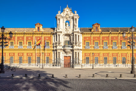 The Palace of San Telmo in Seville town, capital of Andalusia in Spain. Grand palace facade with ornate details, under a bright blue sky. Flags fly freely.の写真素材
