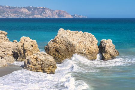 Nerja town, a resort of The Costa del Sol seaside region in Andalusia in the south of Spain. Ocean waves crashing against coastal rocks, a scenic view of turquoise water and distant mountains.の写真素材