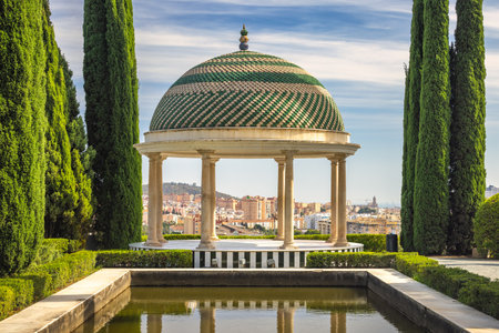 The Historical Botanical Garden La Concepcion in Malaga city at Andalusia, Spain, Europe. Elegant gazebo with a dome, overlooking a city from a manicured garden.の写真素材