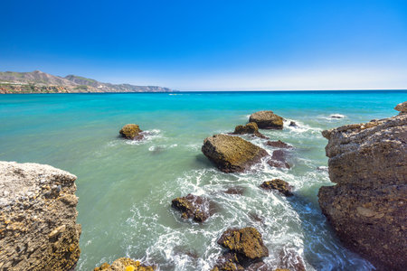 Nerja town, a resort of The Costa del Sol seaside region in Andalusia in the south of Spain, view from the Balcon de Europa square. Stunning turquoise ocean with rocky shoreline under a blue sky.の写真素材