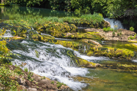 Kocusa waterfall in village Veljaci, Bosnia and Herzegovina, Europe. Scenic waterfall cascading over mossy rocks, surrounded by lush greenery on a sunny day. Beautiful natural landscape.の写真素材