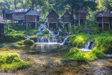 The Mlincici wooden watermills at Pliva river near Jajce town in Bosnia and Herzegovina, Europe. Historic watermills stand along a cascading stream, lush with greenery.の写真素材