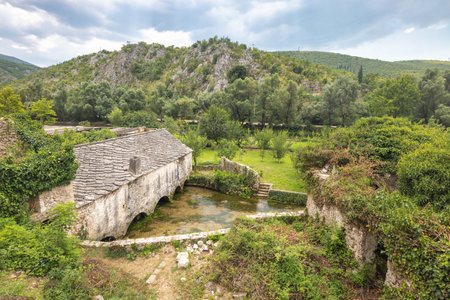 Old stone house in Blagaj village in Bosnia and Herzegovina, Europe. Historic stone building with arched openings over a small river, surrounded by lush greenery and a scenic landscape.の写真素材