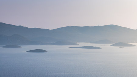 Serene ocean view featuring small islands scattered near the coast, backed by hazy mountains....