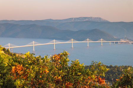 The Peljesac Bridge to Peljesac peninsula in Croatia, Europe. Panoramic view of a long suspension bridge stretching across a body of water with mountains in the background, scenic landscape.の写真素材