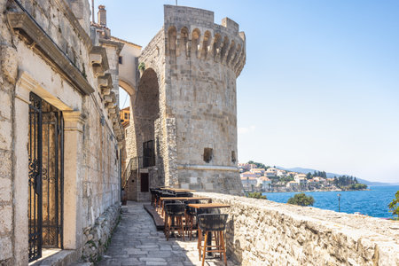 Korcula town in island of Korcula in Adriatic sea in Croatia, Europe. Coastal view with historic stone architecture featuring a prominent medieval tower, tables and sea backdrop.の写真素材