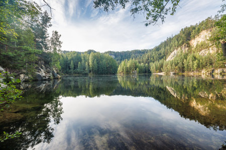 The Piskovna lake in Adrspach-Teplice Rocks area, in Hradec Kralove Region in the Czech Republic, Europe. Reflections of trees and sky create a serene scene on the tranquil waters of the lake.の写真素材