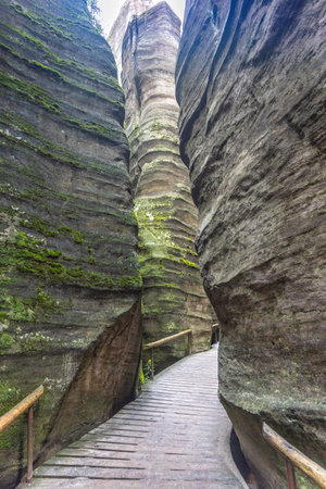 Adrspach-Teplice Rocks, sandstone formations in Hradec Kralove Region in Czech Republic, Europe. A wooden walkway winds through a narrow gorge, surrounded by towering rock formations covered in moss.の写真素材