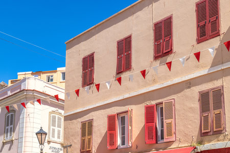 Gibraltar, United Kingdom - September 10, 2024: Mediterranean architecture with red and beige shutters, festive bunting adorns the buildings under a bright blue sky.のeditorial素材