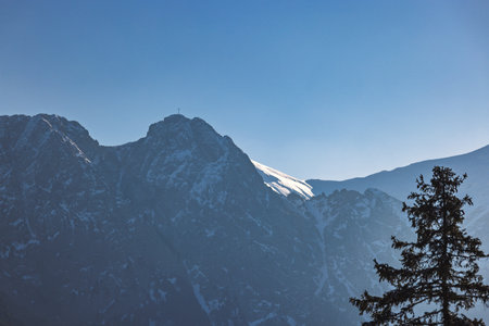 Giewont peak in Tatra Mountains above Zakopane town in Poland, Europe. A majestic mountain peak crowned with snow, piercing the clear blue sky, captured in a scenic mountain landscape.の写真素材