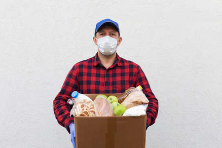 the volunteer in a protective mask with a box of food, donation