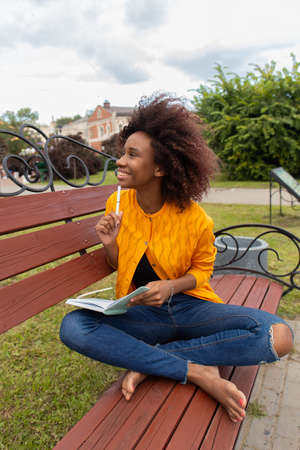 the Beautiful and happy African American woman in the park, makes notes in a notebookの写真素材
