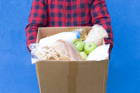 the volunteer with a box of food on a blue background, donations