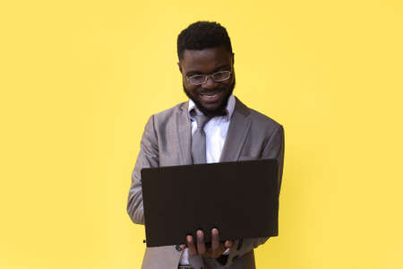 an Image of happy excited young african man isolated over yellow background using laptop computer.の写真素材