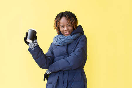 the Happy African American in winter clothes on a yellow background