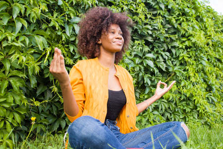 happy and young African American woman meditates on the grass