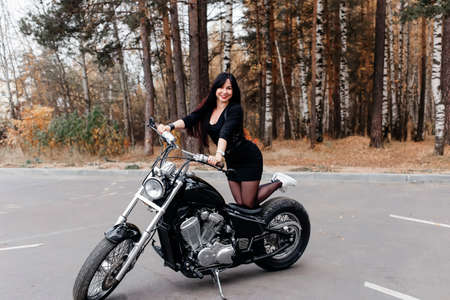 the beautiful brunette in a dress on a motorcycle in the parkの写真素材